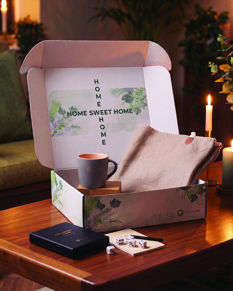 Geschenkset Home Sweet Home: Geschenkbox mit Decke, Tasse und Tischspiel auf dem Couchtisch