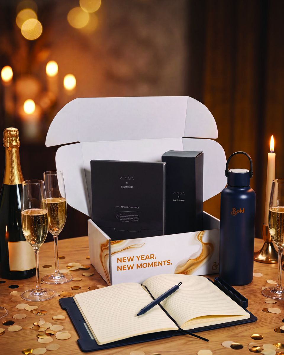Geschenkset New Year Start-Up Specials: Geschenkbox mit Flasche und Notizbuch zwischen Sektgläsern und Kerzen